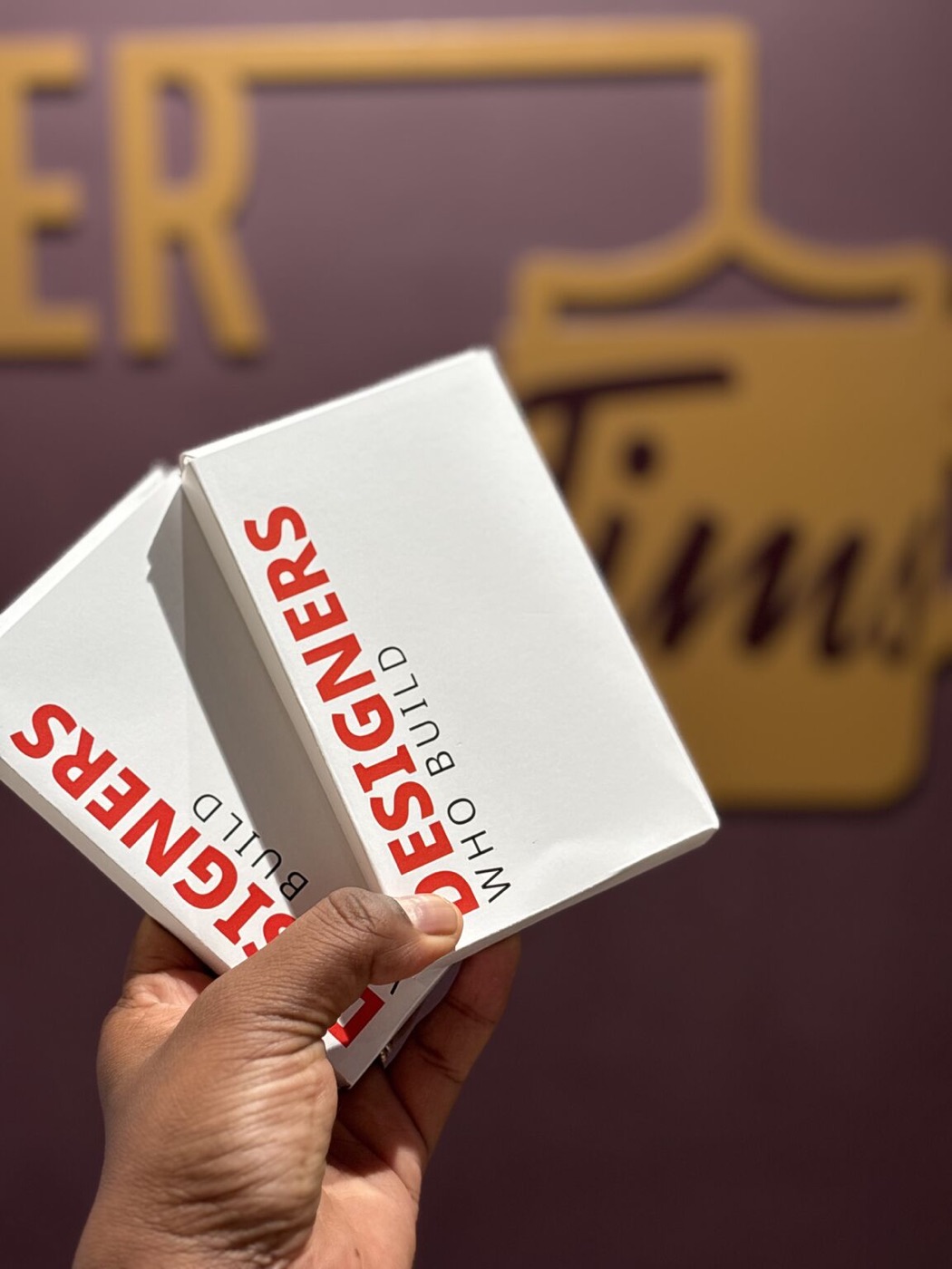 Two Designers Who Build card deck boxes, held up in one hand